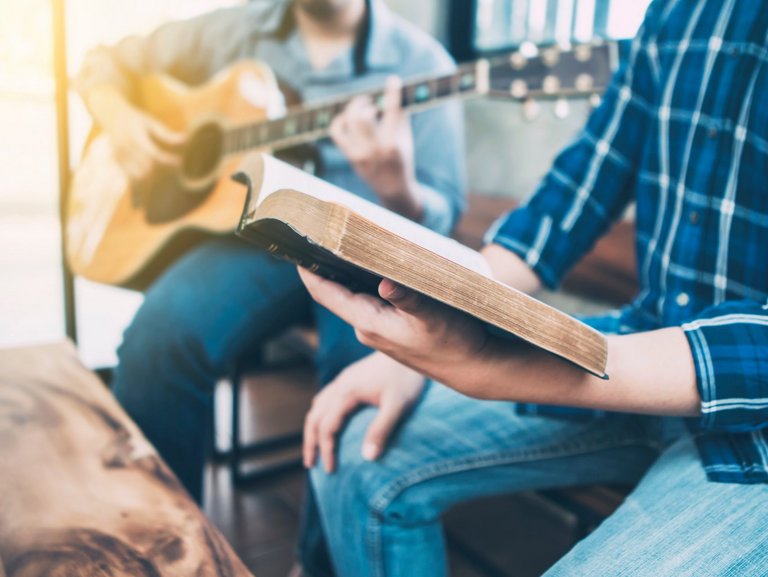 Nahaufnahme zweier Männer, die musizieren - einer mit Gitarre, einer mit Gesangbuch